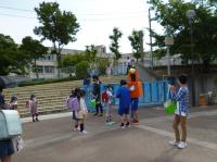 中学生が小学校の正門であいさつ運動兼緑の羽根募金活動をしています。